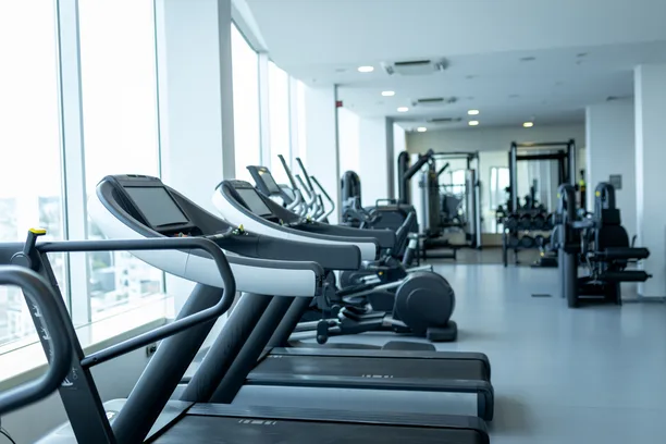A row of treadmills beside tall windows on a bright gym floor, with more machines in the background — gym and fitness studio insurance in Wyoming