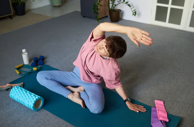 A person seated on an exercise mat leaning into a side stretch, with a foam roller, water bottle and resistance bands nearby — gym and fitness studio insurance in Alabama