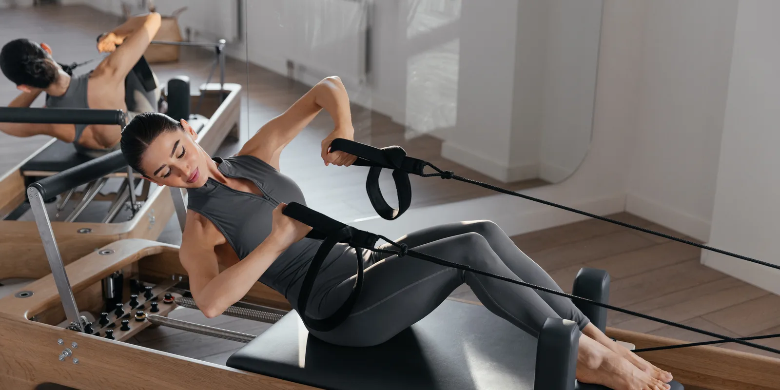 A person lying back on a reformer carriage and drawing the handles in a bright studio — gym and fitness studio insurance in Oregon