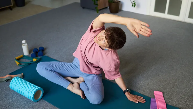 A person seated on an exercise mat leaning into a side stretch, with a foam roller, water bottle and resistance bands nearby — gym and fitness studio insurance in Missouri