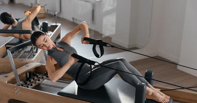 A person lying back on a reformer carriage and drawing the handles in a bright studio — gym and fitness studio insurance in North Carolina
