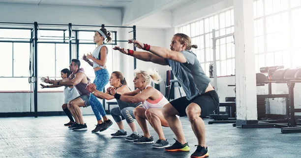 A group of people in athletic wear squatting in unison with arms extended forward on a bright gym floor — gym and fitness studio insurance in Nevada