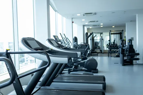A row of treadmills beside tall windows on a bright gym floor, with more machines in the background — gym and fitness studio insurance in New Mexico