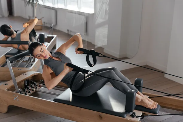 A person lying back on a reformer carriage and drawing the handles in a bright studio — gym and fitness studio insurance in Delaware