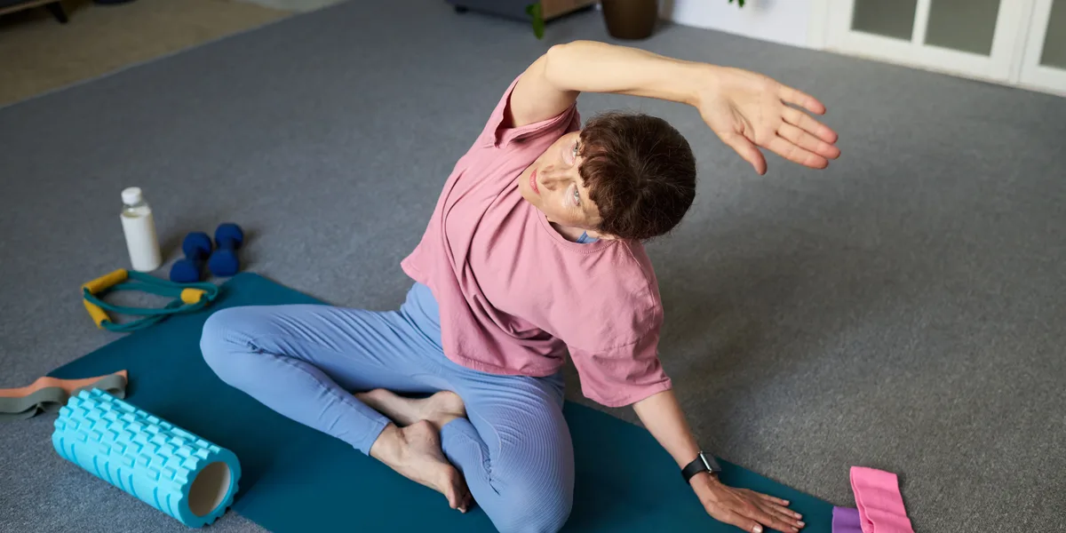 A person seated on an exercise mat leaning into a side stretch, with a foam roller, water bottle and resistance bands nearby — gym and fitness studio insurance in Maine